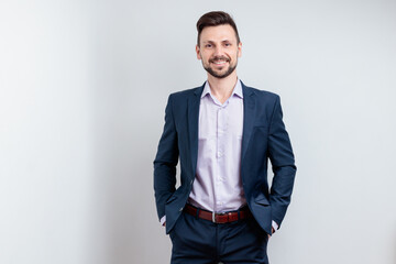 Image of happy brunette man wearing suit smiling at camera with hands in pockets isolated over gray background