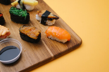 Sushi platter. A selection of raw fish and rice snacks with chopsticks on yellow background.