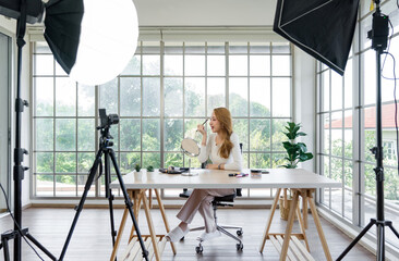 A woman filming her makeup tutorial in a bright room with large window, using a studio setup that...