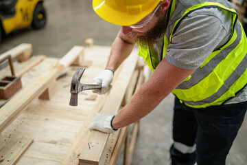 Young adult carpenter hammering nail hardwood at wooden pallet factory. Male industrial engineer...