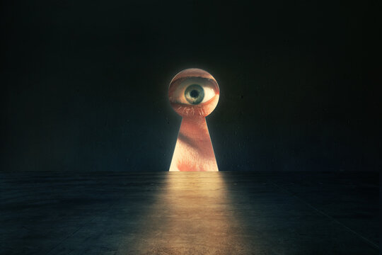 Human eye looking through keyhole in concrete wall in dark room