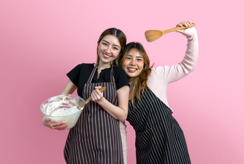 Two women are having fun baking together. They are wearing aprons and smiling while mixing...