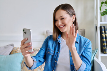 Young woman sitting with smartphone at home having video call