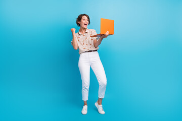 Full size portrait of glad positive girl use laptop raise fist shout yes hooray achievement isolated on blue color background