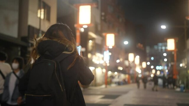 Asian woman tourist using navigation online map on smartphone during at Asakusa district, Tokyo, Japan in winter night. Attractive girl enjoy outdoor lifestyle travel city street on holiday vacation.