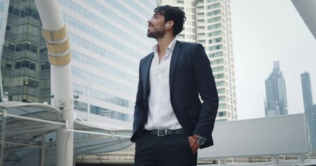 Successful negotiations completed, businessman in formal suit satisfaction. Wide smile and victorious gesture indicate successful. City financial district in background highlights successful deal.