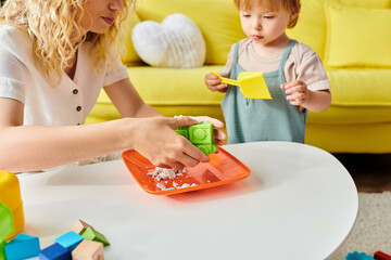 A curly-haired mother engages her toddler daughter in Montessori play, fostering learning and joy in their cozy living room.