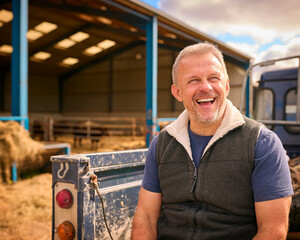 Close Up Of Mature Male Farm Worker Sitting On Tailgate Of Off Road Farm Vehicle