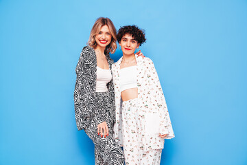 Two young beautiful smiling brunette hipster female in trendy summer costume clothes. Sexy women posing near blue wall in studio. Positive models having fun. Cheerful and happy