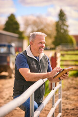 Mature Male Farm Worker Standing Outside Barn Checking Digital Tablet