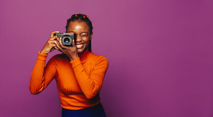 Cheerful young woman capturing vibrant picture on purple background