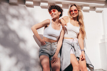 Two young beautiful smiling hipster female in trendy summer white t-shirt and shorts clothes. Sexy...
