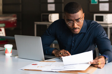Serious and focused financier accountant on paper work inside office, mature man using calculator and laptop for calculating reports and summarizing accounts, businessman at work in casual clothes.