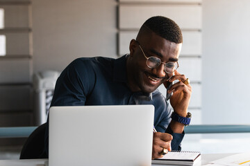 African american casual businessman talking on smartphone sitting at desk in office