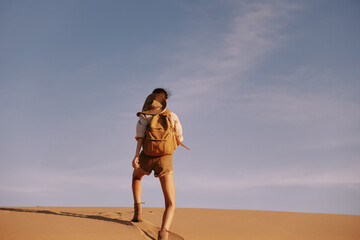 Lonely figure walking on top of sandy dune in vast desert landscape under clear blue sky