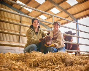 Portrait Of Two Female Farm Workers Checking On Calf In Barn