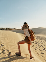 Desert adventure Woman with backpack wandering through sandy dunes on a sunny day in scenic...