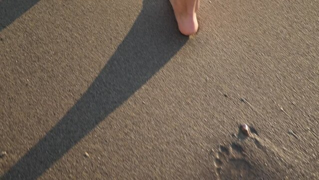 Woman walking and leaving foot traces on sand beach, closeup. Camera moving after girl