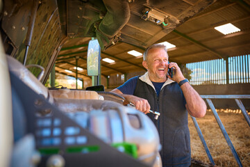 Close Up Of Mature Male Farm Worker On Phone Trying To Fix Machinery