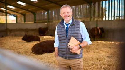 Portrait Of Mature Male Farm Worker Or Manager Standing Inside Cattle Barn With Digital Tablet © Monkey Business