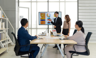 A business meeting in a modern office. A male presenter in suit pointing at digital screen...