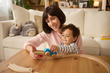 Cute little boy and his mother playing with wooden train at home