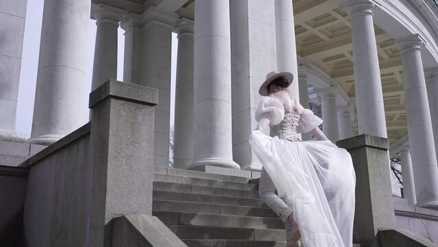 Elegant woman in historical dress gracefully ascends steps of classical building