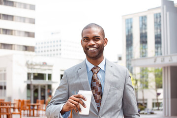Portrait of a smiling handsome businessman with a coffee cup walking down the street on a...