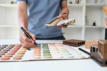 Experienced senior male interior designer choosing paint tone from color swatch samples at office
