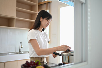 Young beautiful woman standing by the stove, preparing lunch in modern kitchen