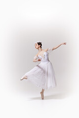 Beautiful ballerina in white dress, performing exquisite ballet move on pointe against white studio background. Concept of art, fusion of classic and modernity, grace and elegance.