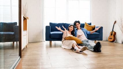 An attractive married man holding a tablet and a woman sit on the floor together in the living room looking at the camera at the new home. A family spends quality time together after home moving.
