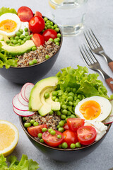 Bowls with healthy salad of quinoa, avocado, legumes, herbs, cherry tomatoes, egg and cream cheese and a glass of water on a light background. The concept of proper nutrition, self-care and health.
