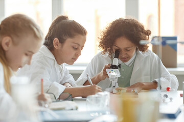 Selective focus shot of ethnically diverse middle school students wearing lab coats using...