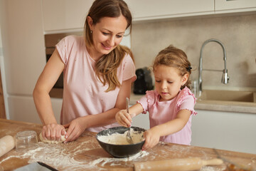 Mother and her daughter kneading dough at wooden table in kitchen