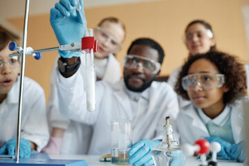 Selective focus shot of young Black teacher and group of ethnically diverse kids doing laboratory...