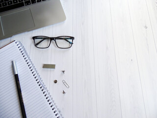 Laptop, notes, okulary i materiały biurowe na białym drewnianym biurku © KJP Photography