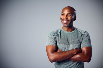 Studio Portrait Of Smiling Mature Man In Gym Fitness Clothing Folding Arms Against Grey Background