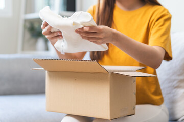 Close-up view of the hands of a young woman opening a cardboard box on the sofa.
