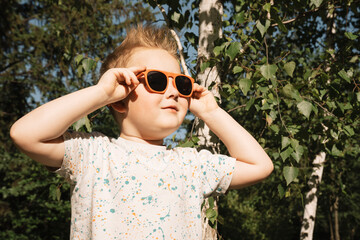 Portrait of a happy child in sunglasses against a background of green trees. Close-up. Happy boy with glasses enjoying the sun. Vacation, summer vacation concept. High quality photo © Дмитрий Загрибаев