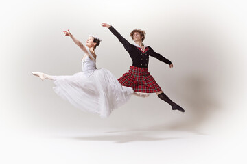 Airborne Elegance. In synchronized leap, ballerina in white dress and floral crown and her partner...