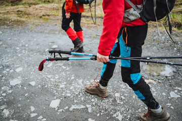Active hikers with trekking poles explore rocky mountain trail in nature. Red jacket, hiking boots,...