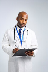 Studio Portrait Of Mature Doctor Wearing White Coat Writing On Patient Chart On Clipboard