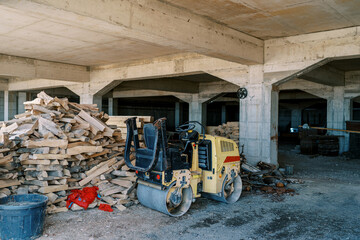 Road roller stands near a pile of firewood in a warehouse