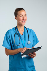 Studio Shot Of Smiling Female Doctor Or Nurse In Scrubs Using Digital Tablet On White Background