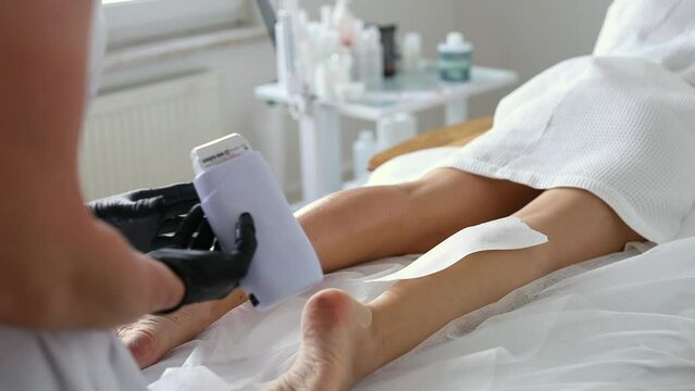 Beautician depilating young woman's legs with liquid sugar in spa center