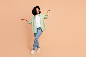 Full length portrait of pretty young woman hold empty space wear shirt isolated on beige color background