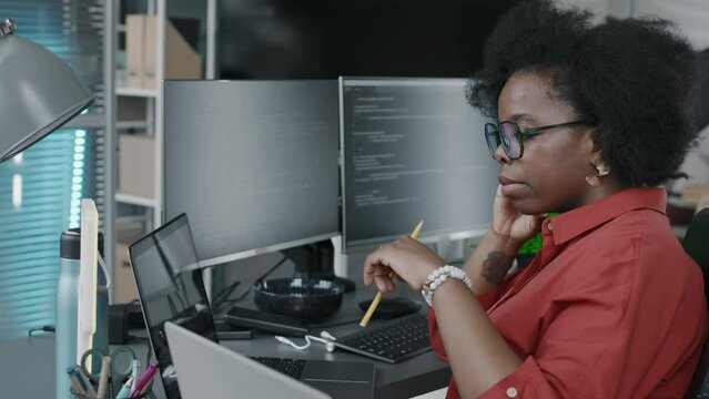 Side view chest up of Black female office employee looking at laptop screen with program codes on it