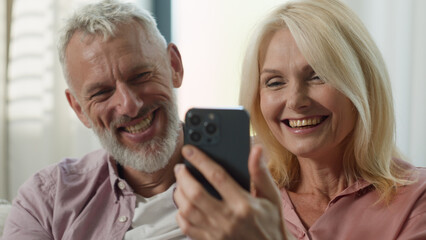 Happy Caucasian couple elderly senior mature wife husband surfing on Internet communicating social...