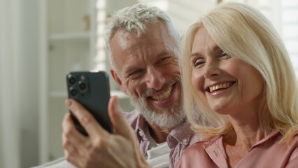 Happy Caucasian couple elderly senior mature wife husband surfing on Internet communicating social...
